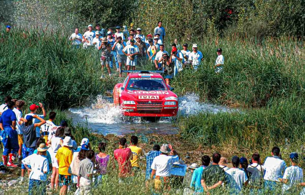 Un coche pasa por un riachuelo rodeado de espectadores