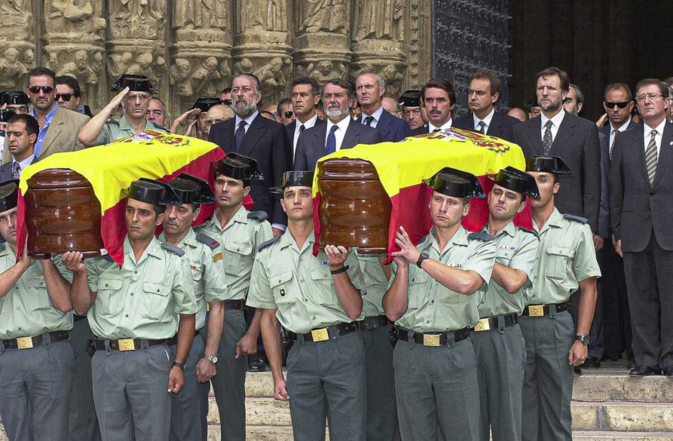 Guardias Civiles sostienes a hombros los féretros con la comitiva política al fondo