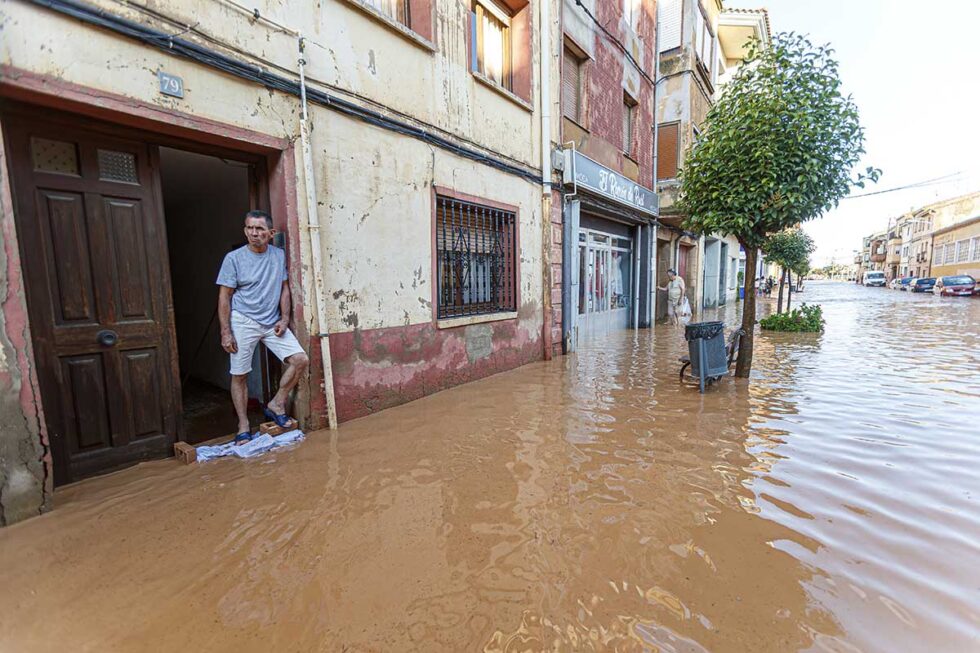 Un hombre asomado a la puerta de su casa y la calle inundada de agua