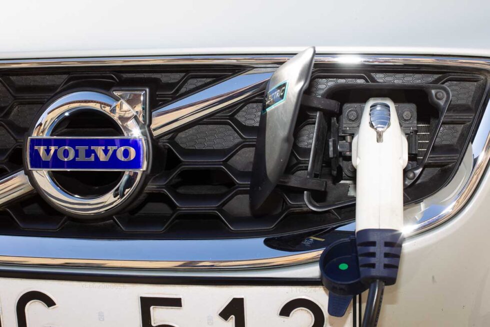 Detalle del primer plano de un cargador enchufado a un coche eléctrico con el logo de Volvo