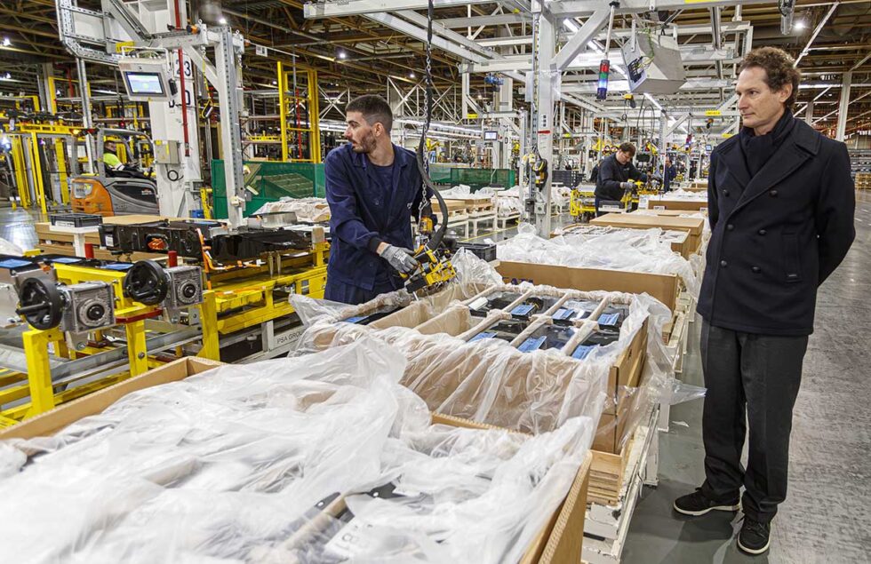 Un supervisor se acerca a revisar la cadena de montaje mientras los trabajadores realizan su trabajo