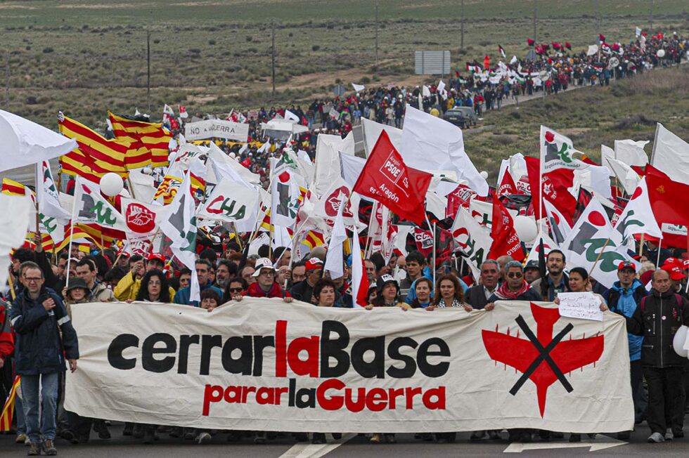 Manifestantes en marcha con diferentes banderas y una pancarta en cabeza con el texto 