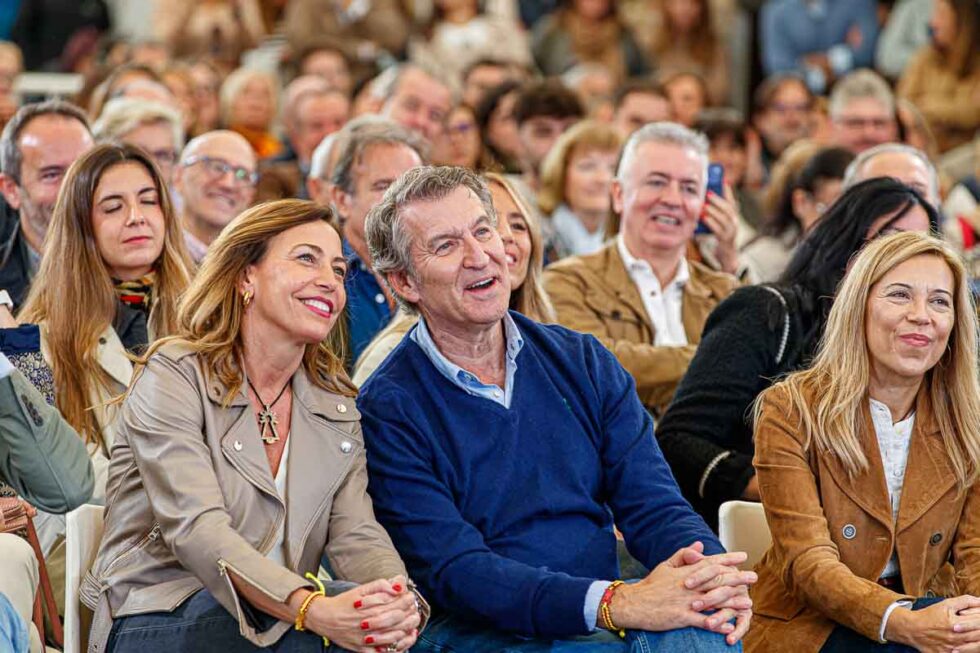 Natalia Chueca y Alberto Núñez Feijoo sonríen sentados en Zaragoza ante un acto del PP
